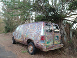Psychedelic custom-painted van, like a unique RV rental, parked off-road by trees.