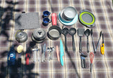 RV rental kitchen setup on a plaid blanket: a complete kit with cookware, dishware, utensils, and cleaning supplies.