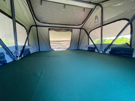 Interior of a roof-top tent, with a comfy green mattress and large windows, perfect for your RV rental adventure.