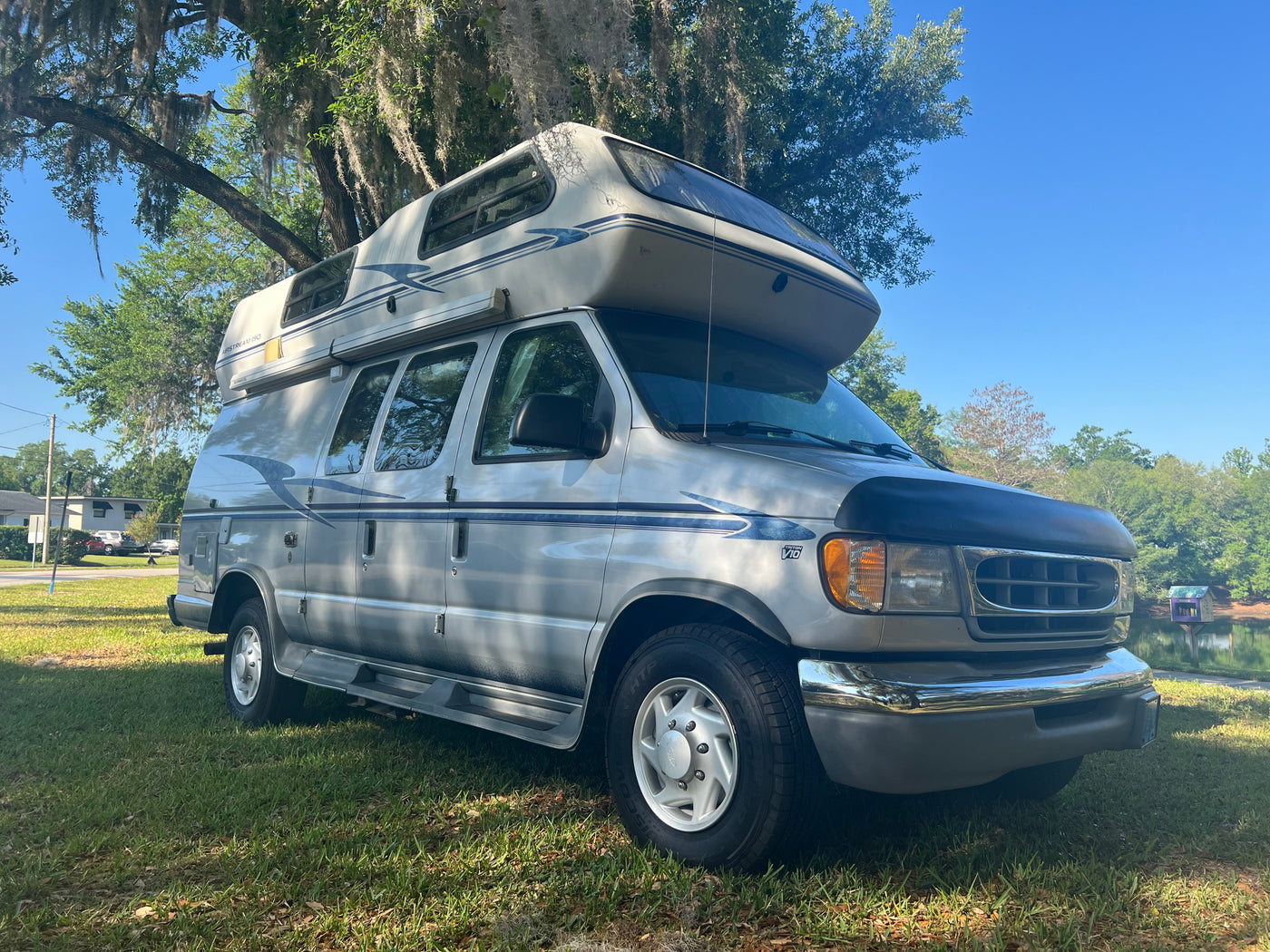 Silver Airstream 190 camper van, ideal for rv rental, parked on grass under mossy trees by a pond on a sunny day. — photo 19