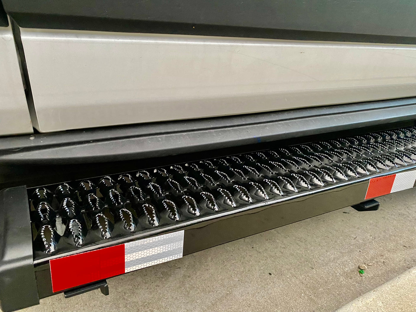 Close-up of a black, textured RV rental step with shiny raised points and red/white reflective strips for safe entry.