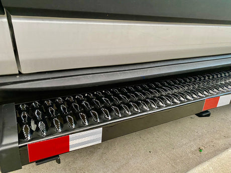 Close-up of a black, textured RV rental step with shiny raised points and red/white reflective strips for safe entry.
