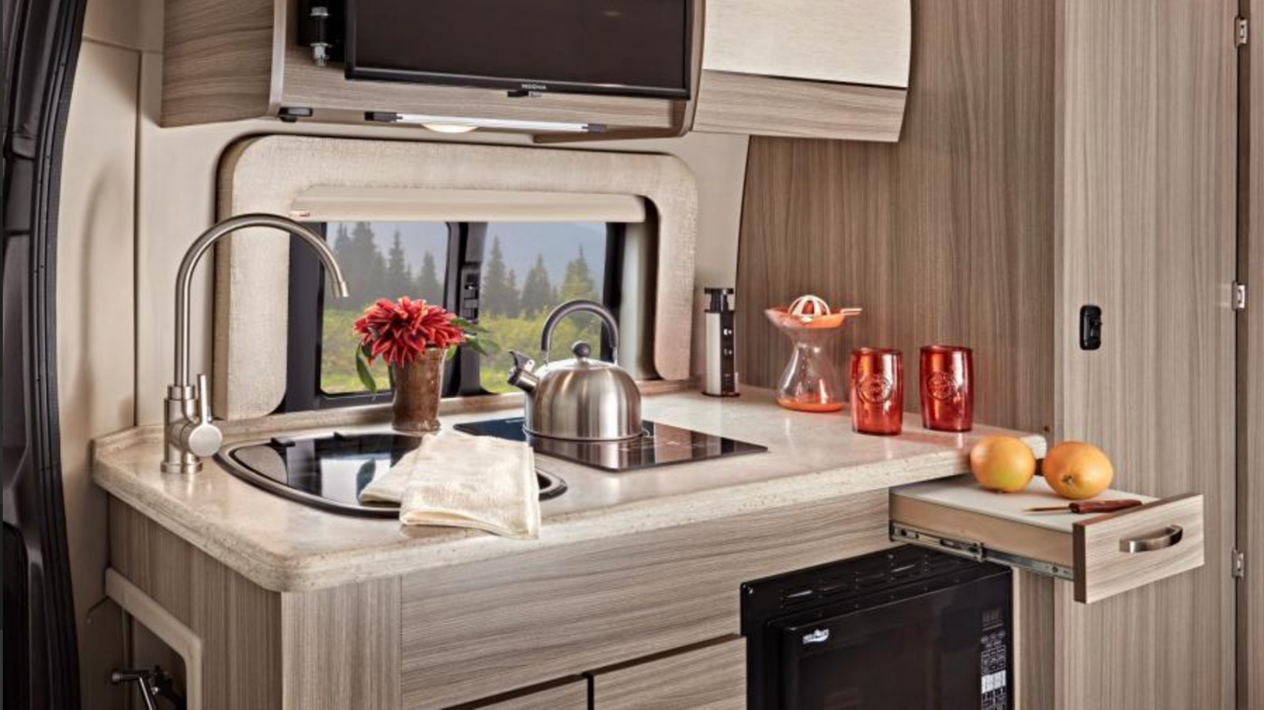 Well-equipped RV rental kitchen with sink, cooktop, microwave, & cabinets. Perfect for mobile living & travel.