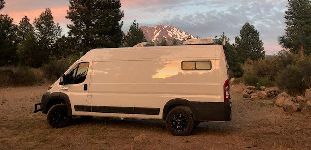 White Promaster camper van for RV rental, parked at sunset against a majestic mountain and trees. — photo 2