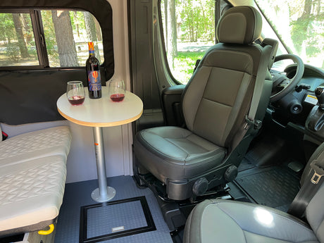 Cozy RV rental interior features wine on a table, a swivel seat, and bench, ideal for relaxed camper van travels.