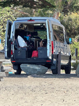 Rear view of a silver RV rental camper van, doors open, revealing a comfortable interior ideal for travel.