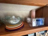 Kitchen essentials neatly stored in an RV rental: nesting glass bowls, colorful plates, and clear organizer bins in a wood cabinet.