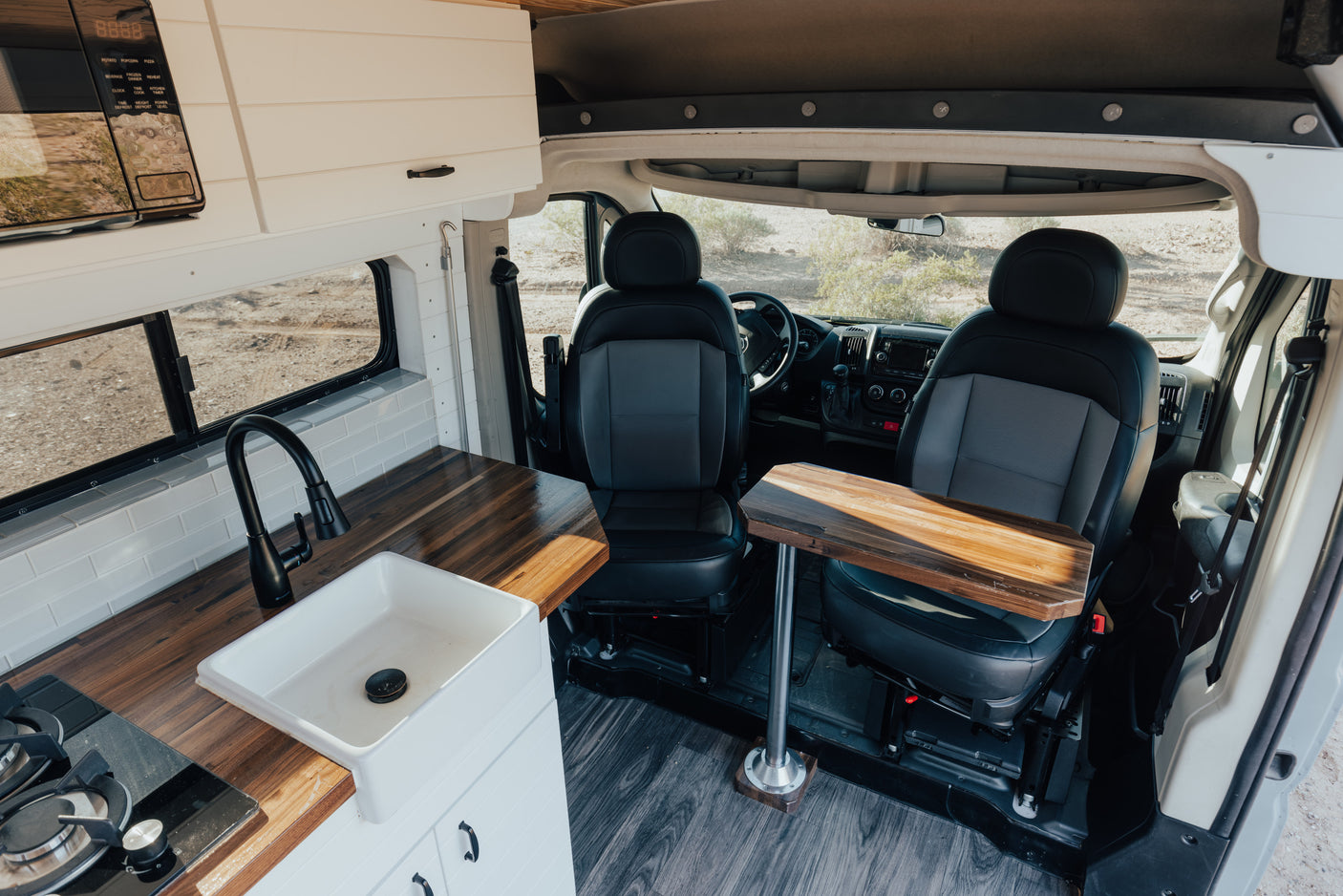 RV rental: Custom camper van interior featuring a sleek kitchen with wooden counters, swivel front seats, and a dining table.