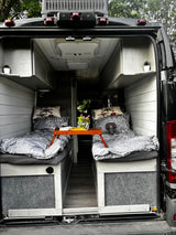 Cozy RV rental interior: twin beds, overhead storage & a charming setup for travel in this customized camper van.