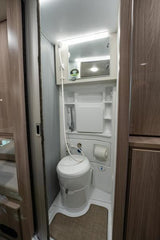 Inside an RV rental, a compact wet bath featuring a toilet, hose shower, small sink faucet, and mirror for essential comfort.