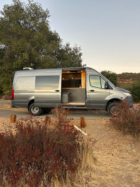 Explore with this sleek grey RV rental van. Its side door is open, showcasing a modern, comfortable interior ready for travel.