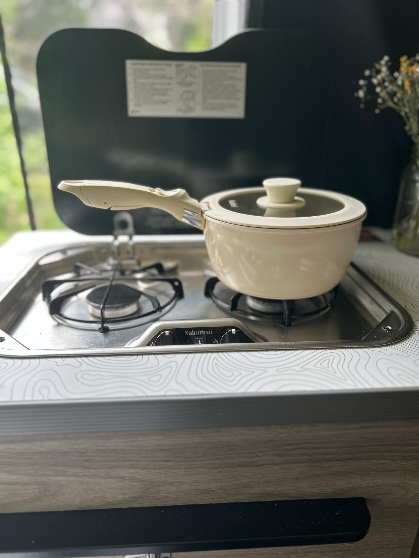 Cooking a meal in an RV rental, featuring a compact Suburban cooktop with a cream pot. Ideal for travel adventures.