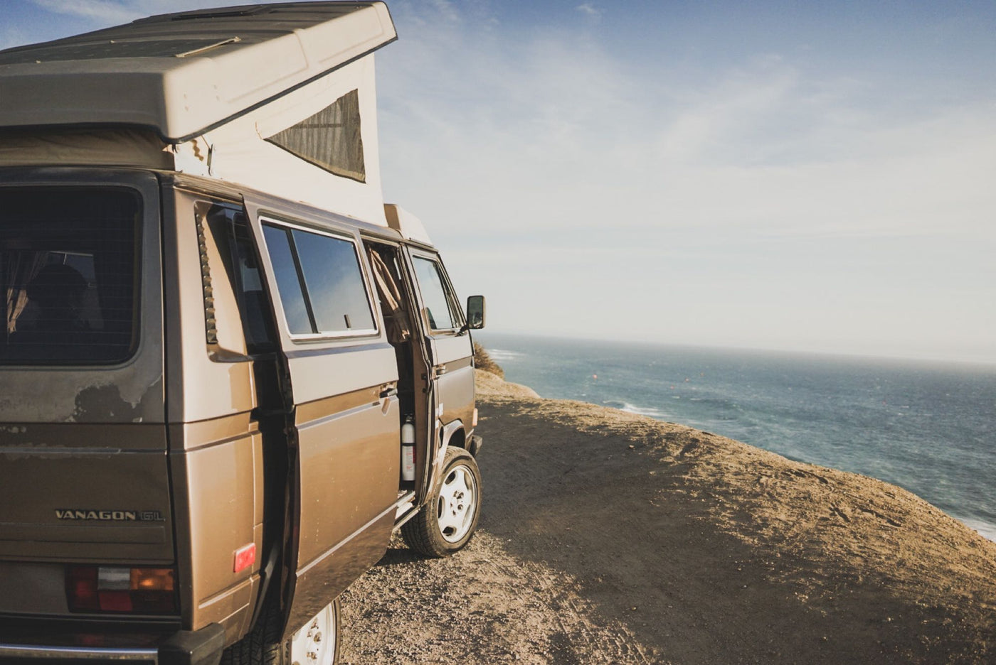  overlooking the ocean at sunset. Relaxing inside a camper van with a stunning view.|This RV rental offers stunning ocean sunset views. A dark pop-top camper van is parked — photo 2