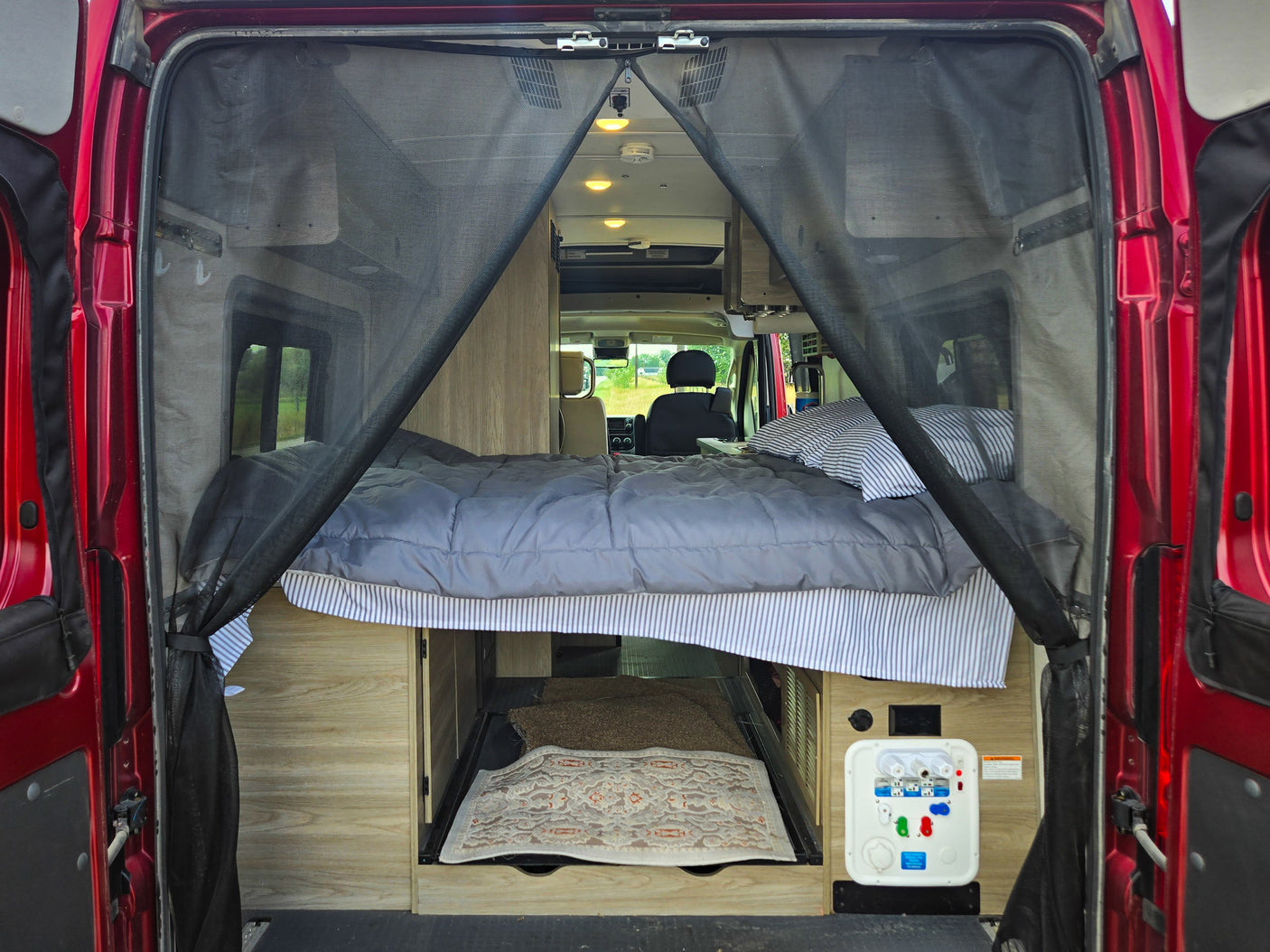 Inside a comfy RV rental: bed, under-bed storage, and utility panel, with a protective bug screen at the rear.