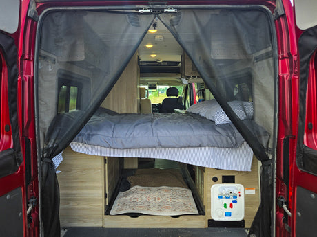 Inside a comfy RV rental: bed, under-bed storage, and utility panel, with a protective bug screen at the rear.