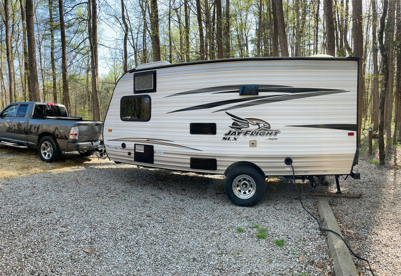 RV rental setup: A Jayco travel trailer hitched to a pickup truck on a gravel campsite amidst trees, perfect for camping. — photo 15