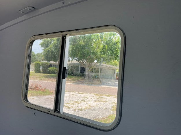 Inside an RV rental, a clear view through the window shows a peaceful suburban street, homes, and trees.