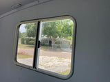 Inside an RV rental, a clear view through the window shows a peaceful suburban street, homes, and trees.