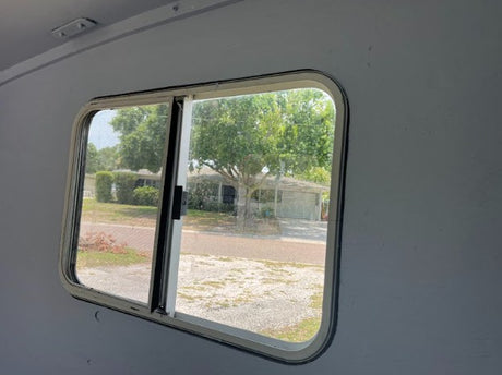 Inside an RV rental, a clear view through the window shows a peaceful suburban street, homes, and trees.