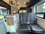 Inside a spacious RV rental: modern kitchen setup, overhead controls, and comfortable black passenger seats.