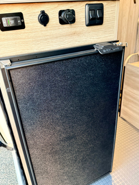 RV rental: Novacool fridge, coach battery switch (on/off), 12V power outlets, and other electrical switches on a wood panel.
