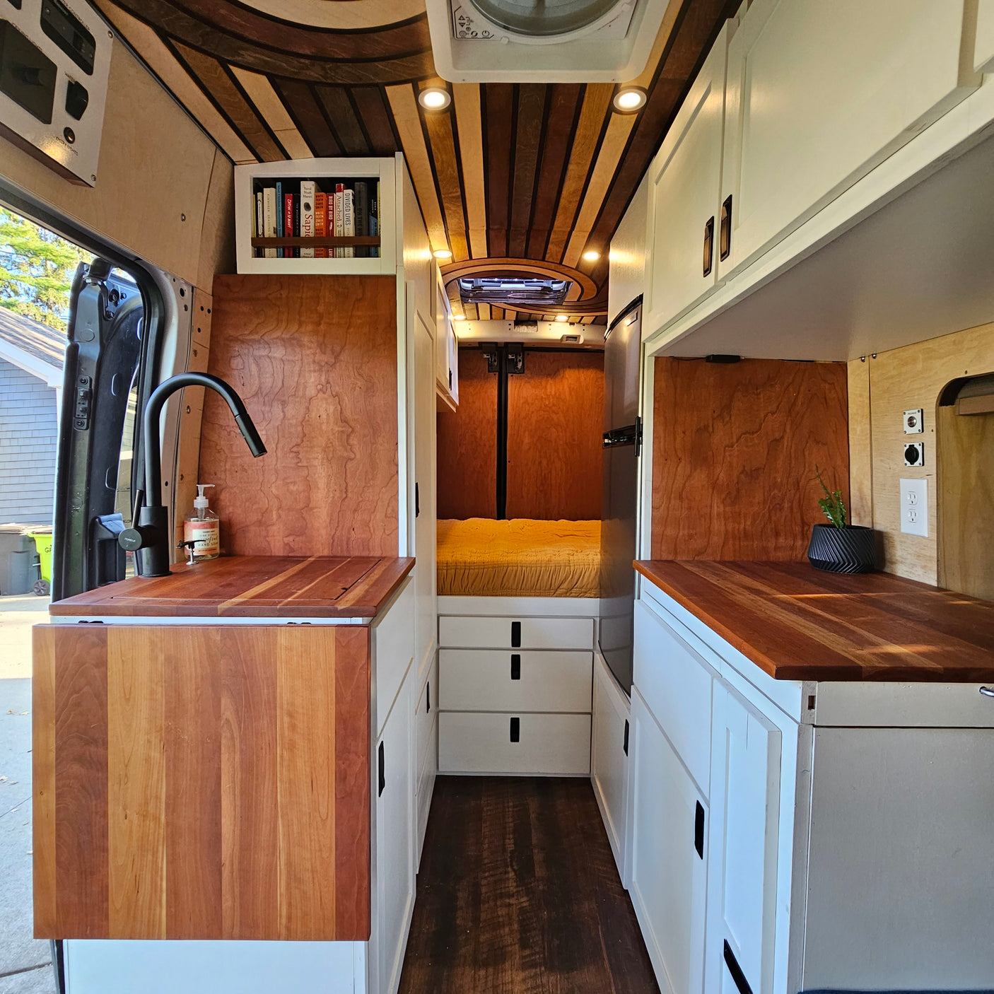 Detailed RV rental: custom camper van interior with wood ceiling, compact kitchen, and bed, perfect for travel.