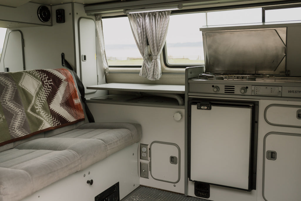 Explore a cozy RV rental interior with a compact kitchen, comfortable bed, and versatile table, ready for your next adventure.