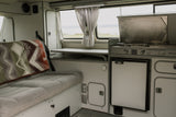 Explore a cozy RV rental interior with a compact kitchen, comfortable bed, and versatile table, ready for your next adventure.