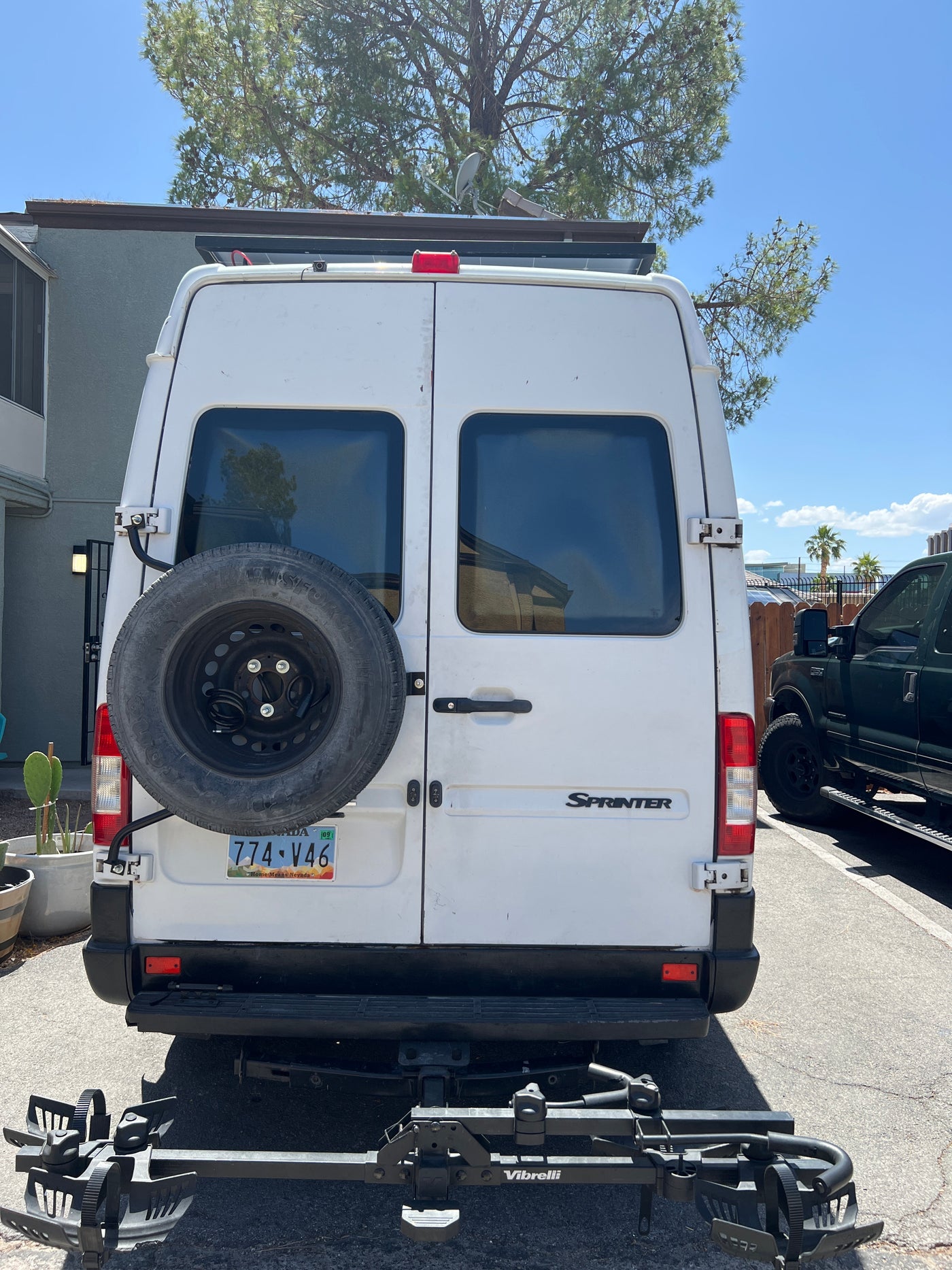 Rear view of a white Mercedes Sprinter van, a common RV rental. It has a spare tire, bike rack, and roof-mounted solar panels. — photo 10