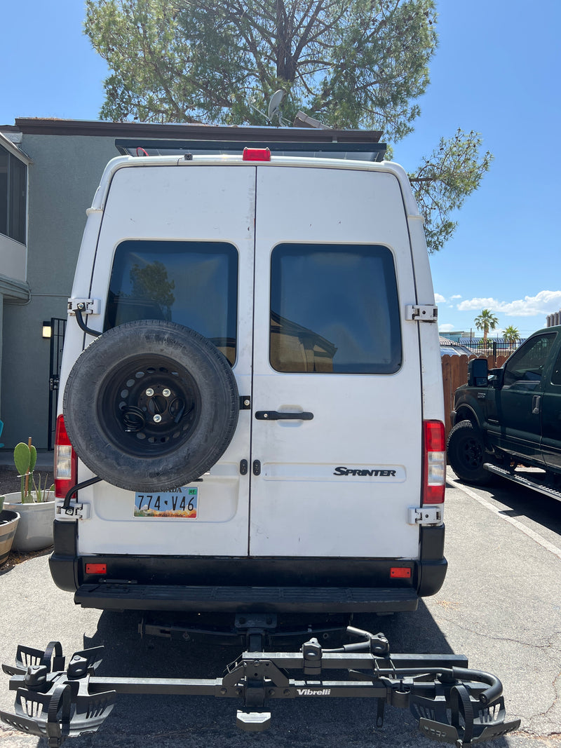 Rear view of a white Mercedes Sprinter van, a common RV rental. It has a spare tire, bike rack, and roof-mounted solar panels. — photo 10
