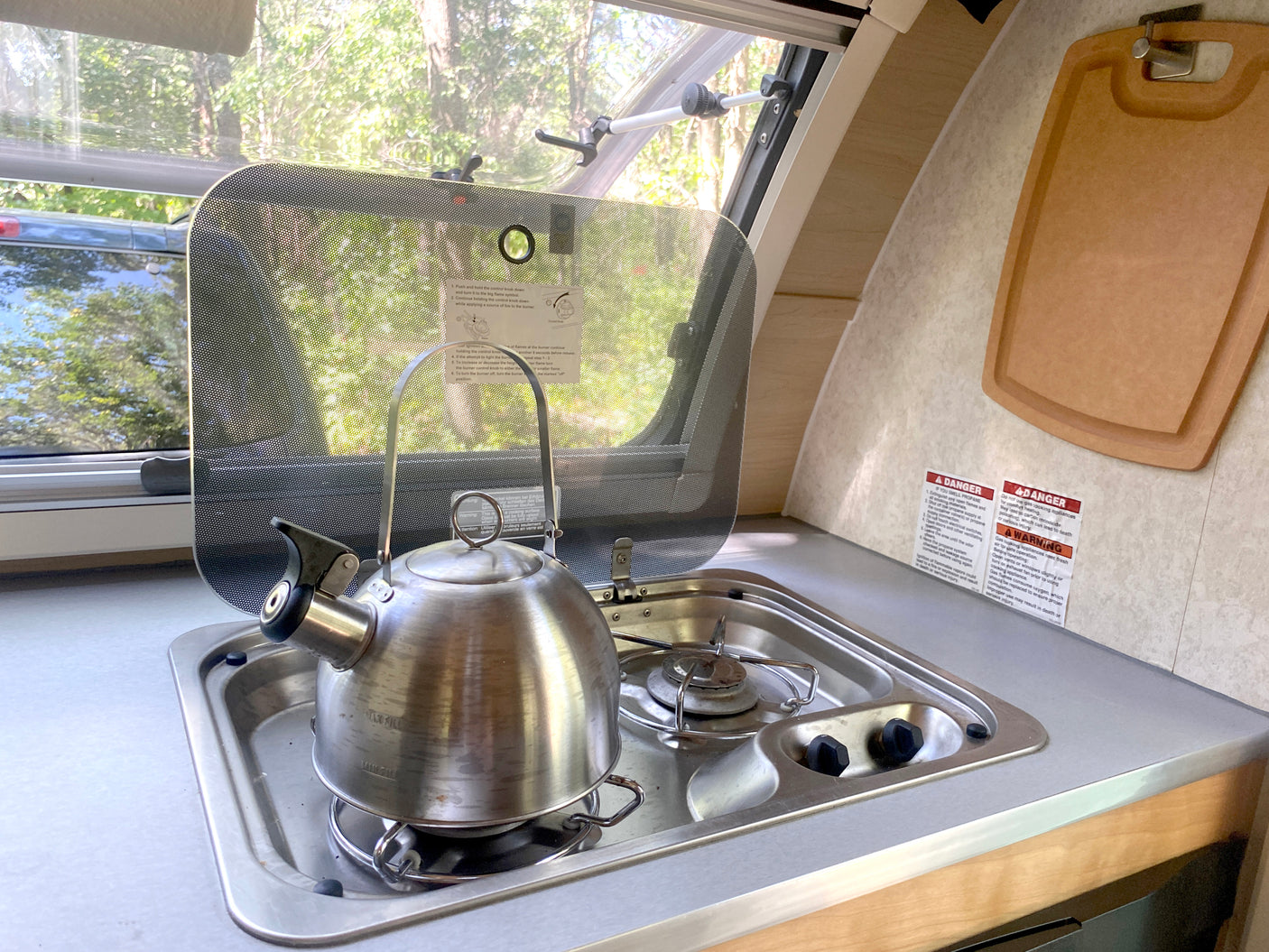 This RV rental features a compact kitchen with a kettle on the stove, sink, and visible safety warnings.