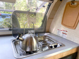 This RV rental features a compact kitchen with a kettle on the stove, sink, and visible safety warnings.