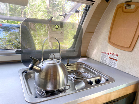 This RV rental features a compact kitchen with a kettle on the stove, sink, and visible safety warnings.