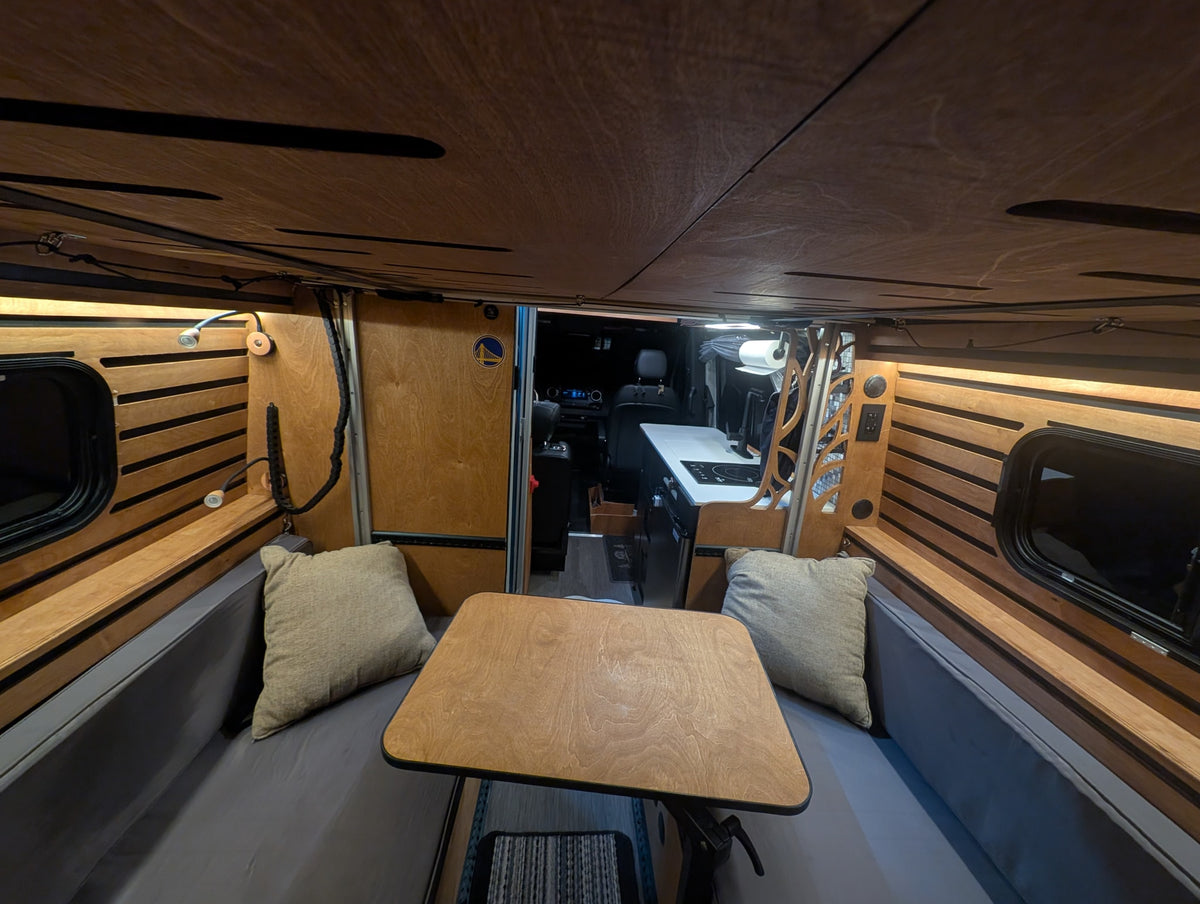 Cozy RV rental interior: A wooden dining table, cushions, and kitchen area are visible in this inviting camper van setup. — photo 15