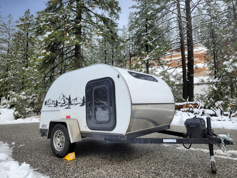  parked on asphalt amidst a snowy forest with pine trees.|Winter wonderland rv rental: A cozy teardrop camper parked in a snowy forest.|Cozy teardrop RV rental ready for adventure — photo 1