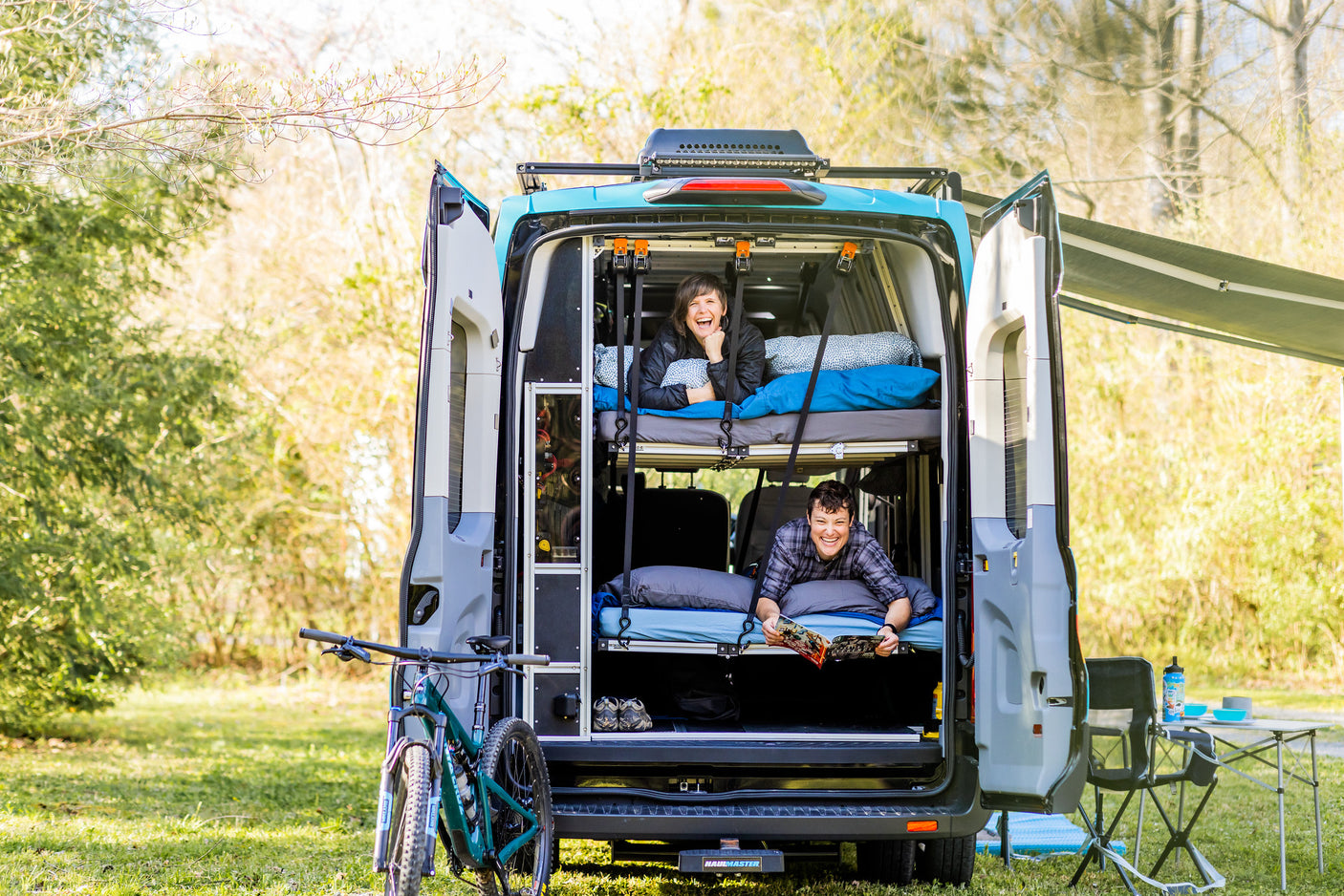Two people relax in their custom RV rental with bunk beds. An outdoor adventure van scene.