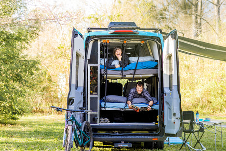 Two people relax in their custom RV rental with bunk beds. An outdoor adventure van scene.