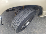An RV rental's front wheel, tire, and suspension components, including a coil spring and yellow shock absorber, on asphalt.