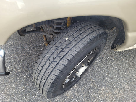 An RV rental's front wheel, tire, and suspension components, including a coil spring and yellow shock absorber, on asphalt.