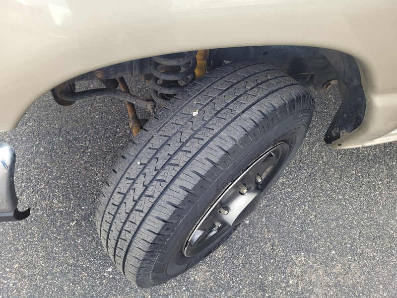 An RV rental's front wheel, tire, and suspension components, including a coil spring and yellow shock absorber, on asphalt. — photo 3