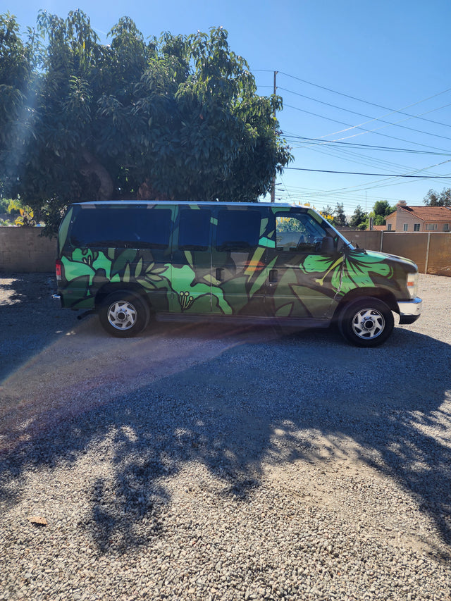 Vibrant green leafy van, great for an RV rental, parked on gravel under a clear sky next to a large tree.