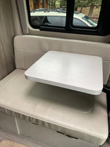 Bright RV rental interior showing a small dining table and bench seating by a window with an outdoor view.