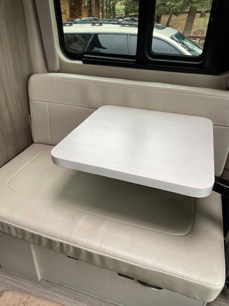 Bright RV rental interior showing a small dining table and bench seating by a window with an outdoor view.