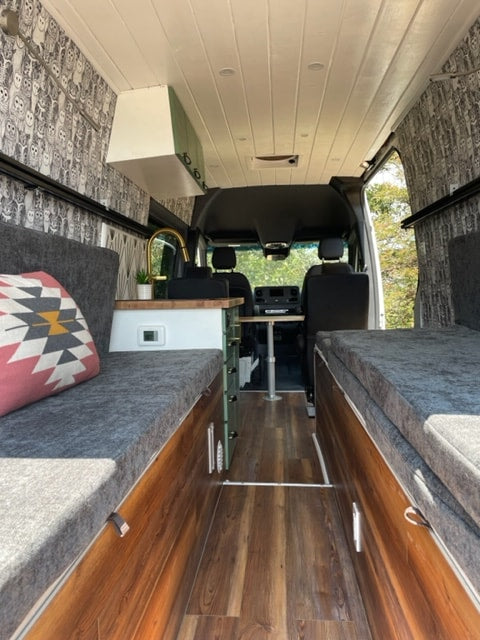 Modern RV rental interior with wood-look flooring, a compact kitchen, and grey upholstered seating. — photo 6