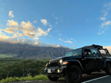 Adventure-ready black Jeep Gladiator RV rental with a rooftop tent, parked on a mountain road with scenic cloudy peaks.