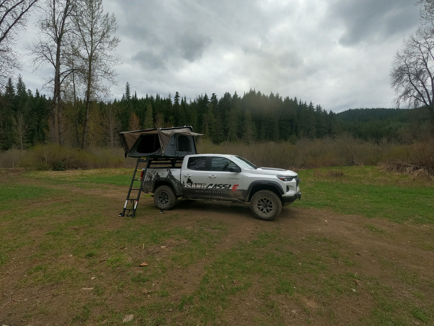White overland truck with rooftop tent setup, available for RV rental in a cloudy forest setting.