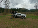 White overland truck with rooftop tent setup, available for RV rental in a cloudy forest setting.