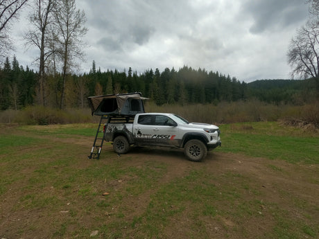White overland truck with rooftop tent setup, available for RV rental in a cloudy forest setting.