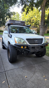 White Lexus GX 470, modified for overlanding with off-road lights, a snorkel, and rooftop tent. Great for an RV rental adventure.