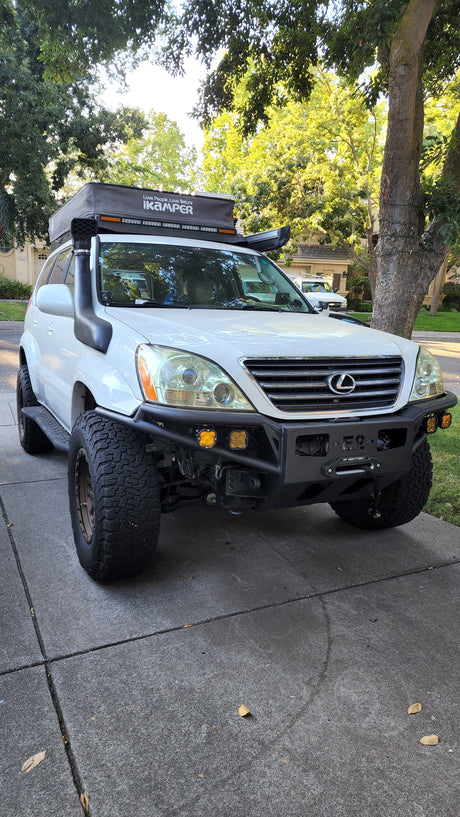 White Lexus GX 470, modified for overlanding with off-road lights, a snorkel, and rooftop tent. Great for an RV rental adventure.